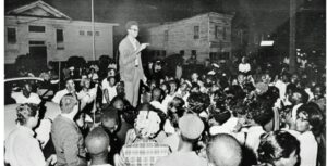 H. “Rap” Brown stands atop a car in the African American section of Cambridge, Md., July 24, 1967 delivering a fiery black nationalist speech denouncing white dominated society and urging African Americans to fight back. Later that night, Brown was wounded by shotgun pellets before he left town. In the early morning hours, someone set fire to an African American school that ended up burning two square blocks while the town’s firemen stood by. Maryland Gov. Spiro T Agnew immediately denounced Brown and he was soon charged with inciting to riot, along with other crimes. The National Guard was again called out to occupy the town. Brown faced other legal woes, but charges in the Maryland case were ultimately dropped several years later. The incident marked the end of the mass civil rights movement in Cambridge that began in 1962. Photo Credit; Washington Area Spark (https://www.flickr.com/photos/washington_area_spark/49222107273/in/album-72157702777400382/)