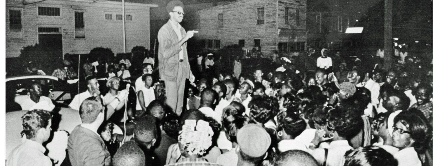 H. “Rap” Brown stands atop a car in the African American section of Cambridge, Md., July 24, 1967 delivering a fiery black nationalist speech denouncing white dominated society and urging African Americans to fight back. Later that night, Brown was wounded by shotgun pellets before he left town. In the early morning hours, someone set fire to an African American school that ended up burning two square blocks while the town’s firemen stood by. Maryland Gov. Spiro T Agnew immediately denounced Brown and he was soon charged with inciting to riot, along with other crimes. The National Guard was again called out to occupy the town. Brown faced other legal woes, but charges in the Maryland case were ultimately dropped several years later. The incident marked the end of the mass civil rights movement in Cambridge that began in 1962. Photo Credit; Washington Area Spark (https://www.flickr.com/photos/washington_area_spark/49222107273/in/album-72157702777400382/)