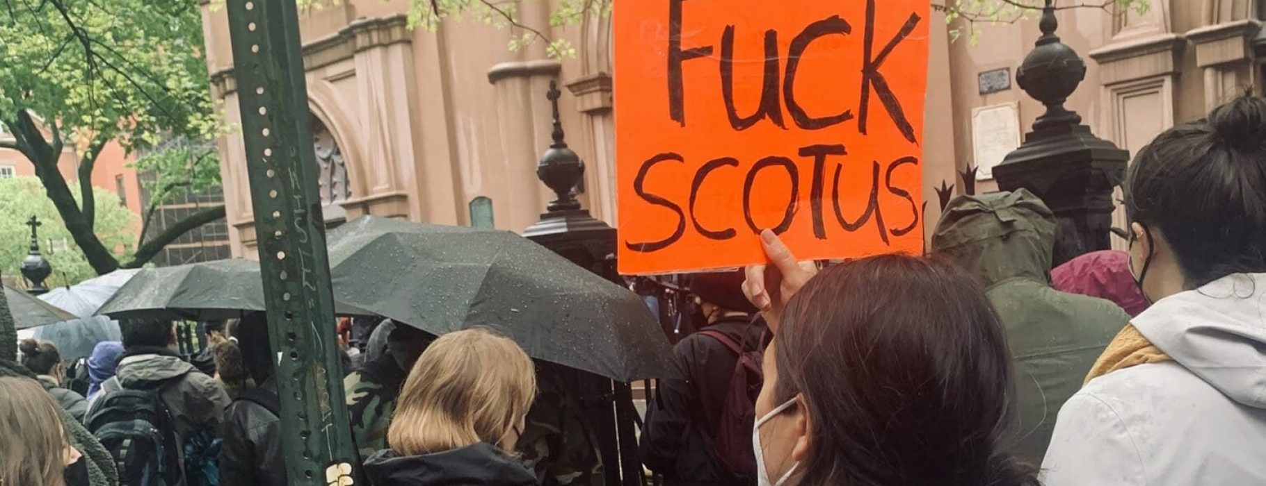 A group on the street protests the leaked memo overturning Roe v. Wade. One protester holds an orange sign that reads 'Fuck Scotus'